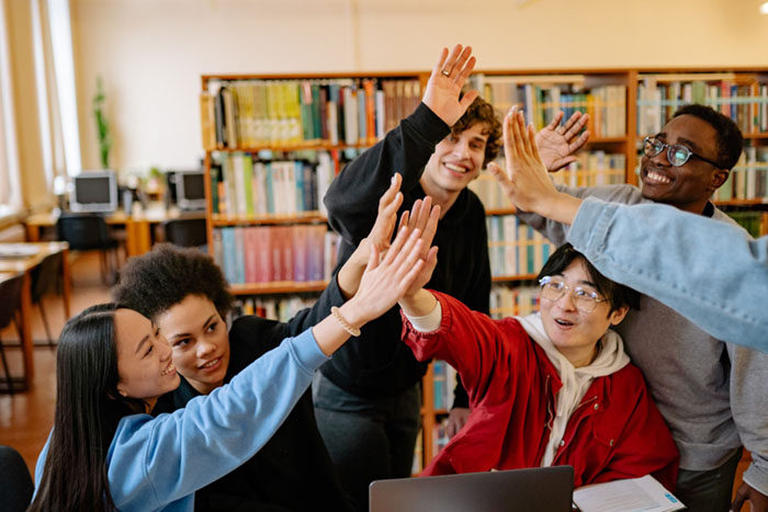 Group of 6 students doing a high five in library